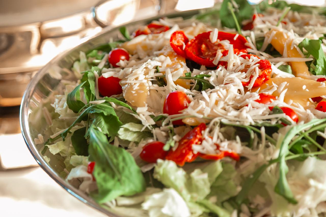 Salada com tomates e queijo branco visíveis, apresentada em travessa de prata